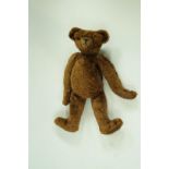 A straw filled teddy bear, with brown plush fur and felt pads,