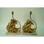 A pair of lamps in the form of gilded cherubs riding swans on a composite 'marble' plinth,