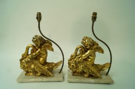 A pair of lamps in the form of gilded cherubs riding swans on a composite 'marble' plinth,