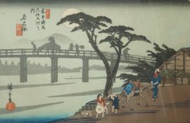 A 20th century Japanese woodblock print of figures on the riverbank with a bridge beyond, p.
