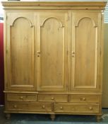 A pine triple wardrobe with three panelled doors above and arrangement of five drawers on turned