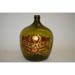 A green glass carboy, printed in red, black and gilt with cartouche titled "Cocaine", overall 47.