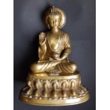 A cast brass study of a seated Tibetan Buddha, his right palm raised, depicted with a halo behind