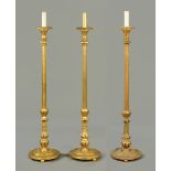 * A set of three carved and giltwood lamp standards, candle form tops,