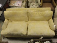 A three seater sofa in pale yellow foliate patterned upholstery, on turned wooden legs to brass