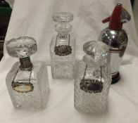 Three cut glass decanters, one with white metal collar, together with two silver wine labels,