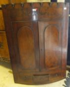 An early 19th Century mahogany bow fronted hanging corner cupboard with two arched panelled doors