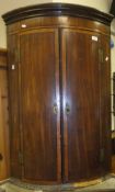 An early 19th Century mahogany and cross-banded bow fronted hanging two door corner cupboard