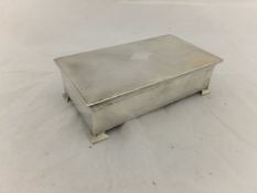 A George V silver cased cigarette box with engine turned decoration to top and raised on four