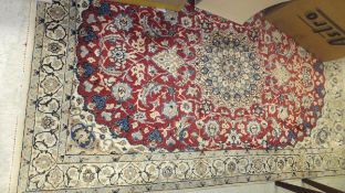 A Qum rug, the central medallion in blue, cream and brown, on a dark red floral decorated ground,