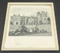 A framed and glazed image of the Royal Family and corgis upon a tartan rug before Balmoral adapted