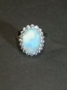 A dress ring, the central opal surrounded by simulated diamonds set on a yellow metal mount,