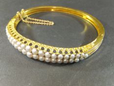 A late 19th Century half pearl hinged bangle of two rows of graduated half pearls set on a pierced