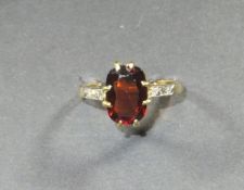 A 22 carat gold and garnet set dress ring, the single stone flanked by diamond set shoulders,