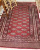 A Bokhara rug, the central dark red ground with repeating elephant foot medallions in pale gold,