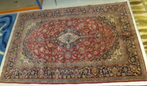 A Kashan rug with central blue lozenge medallion on a red foliate decorated ground within a blue