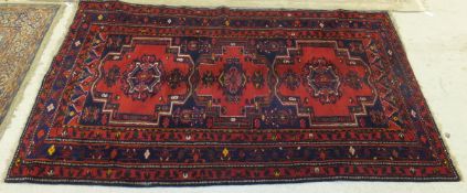 A Persian carpet with repeating medallions on a red ground within a blue and red banded floral