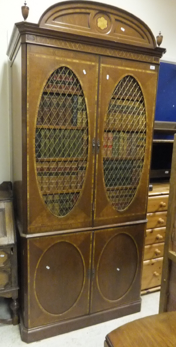 A mahogany and inlaid cabinet with two grilled doors enclosing faux books over two further oval