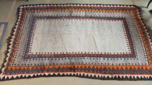 A faux tribal rug, the central cream ground within blue, red, grey,