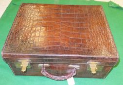 A vintage crocodile skin suitcase with brass fittings opening to reveal a suede-lined interior