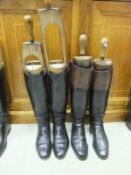 A pair of black and tan leather riding boots with wooden trees and turned handles, together with