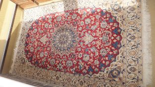 A Qum rug, the central medallion in blue, cream and brown, on a dark red floral decorated ground,
