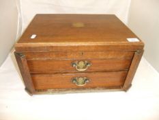 An early 20th Century oak canteen with lift-up lid above two drawers with brass swing handles (no