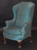 An early 20th Century wing back scroll armchair in the George II taste upholstered in teal fabric,