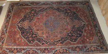 A Persian rug, the central medallion in salmon, blue and green on a dark blue,