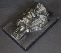A bronzed spelter figure of a sleeping putto upon cross, on a black slate base, base 12.5 cm long (