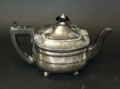A George V silver teapot of rounded rectangular form, raised on four ball feet (by Hemming & Co.