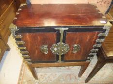 A Chinese engraved brass bound elm and ebonised cupboard, the two doors enclosing a bank of 12