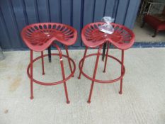 A pair of red painted metal stools in the form of tractor seats*