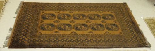A Bokhara rug, the central elephant foot medallions in black and madder on a dark gold ground,