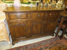 An oak sideboard with three drawers above three panelled cupboard doors,