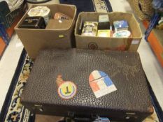 Two boxes containing various vintage tins, and a vintage suitcase bearing paper labels, etc.