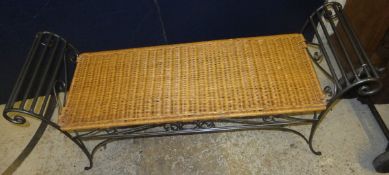 A wrought iron two seat bench with scrolled arms and wicker seat