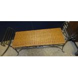 A wrought iron two seat bench with scrolled arms and wicker seat