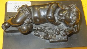 A bronzed spelter figure of a sleeping putto upon cross, on a black slate base (believed to be