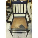 A circa 1900 ebonised framed elbow chair on turned and ringed legs united by stretchers