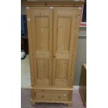 A modern pine wardrobe with double panel doors and drawer below