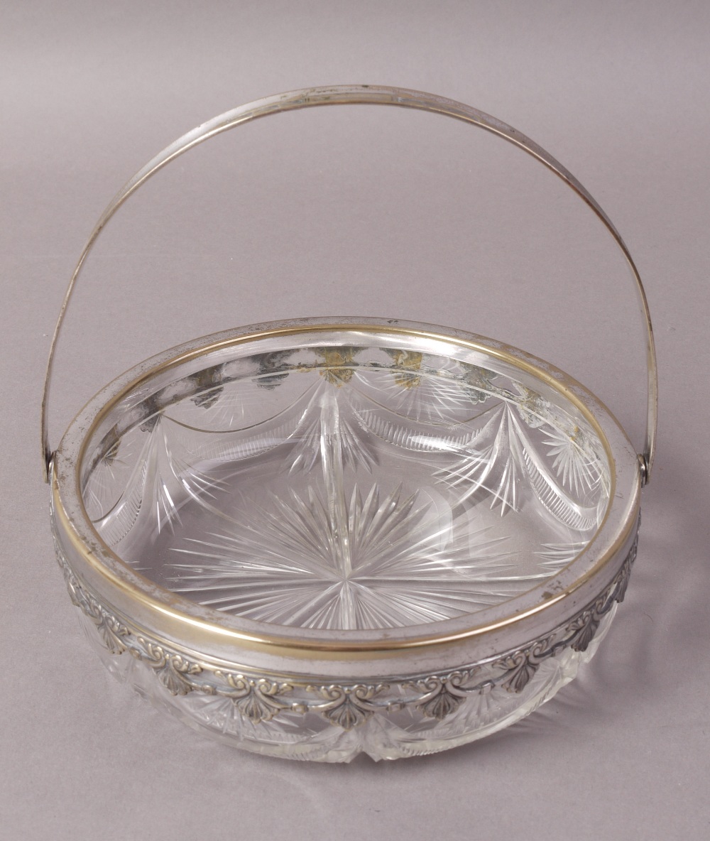 A SILVER PLATED AND CUT GLASS BASKET, circular with swing handle, the rim with pendant anthemion,