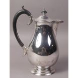 A SILVER HOT WATER JUG OF BALUSTER FORM WITH EBONISED HANDLE raised on a pedestal foot,