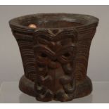 A MAORI CARVED WOODEN VESSEL, of waisted form, carved with Tiki masks on a lined and beaded ground,