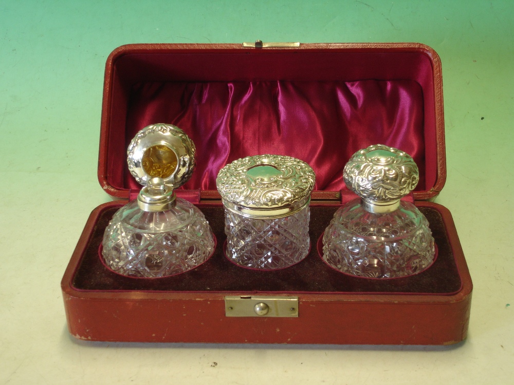 A Cased Dressing Table Set. The pair of cut glass Cologne bottles with repousse silver lids and