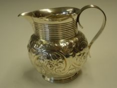 A Silver Jug With repousse decoration of scrolling foliage and an engraved cartouche, reeded neck