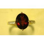 A Garnet Solitaire Ring With an oval stone and four diamonds to each shoulder. In gold marked 375.