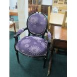AN EBONISED AND UPHOLSTERED ELBOW CHAIR the oval upholstered back and seat on cylinderical tapering