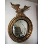 A GILT FRAMED CONVEX MIRROR with ball decoration surmounted by a winged eagle