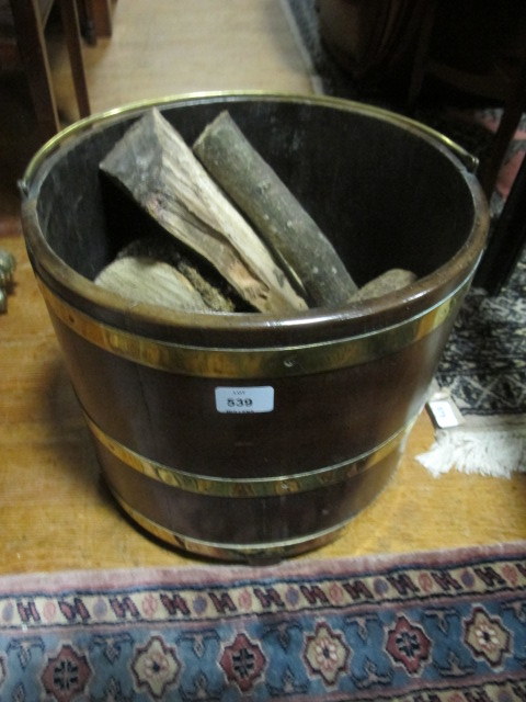A GEORGIAN STYLE MAHOGANY AND BRASS BOUND BUCKET of oval outline with brass swing handle on moulded
